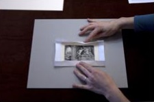 1. Corta un trozo de papel más grande que la obra, al menos, 2,5 cm en todos los bordes. Dobla el papel alrededor de la obra.